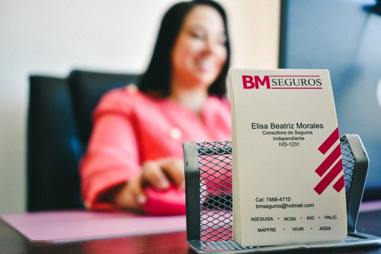 Tarjeta de presentación de Elisa Beatriz Morales, consultora de seguros, con una mujer desenfocada detrás.
