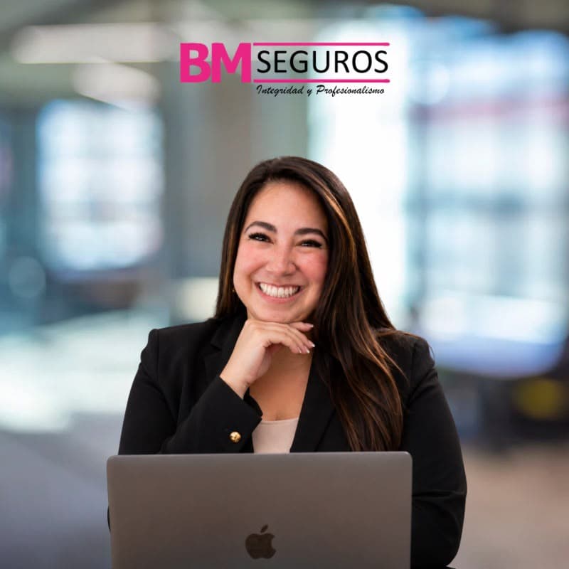 Representante de BM Seguros sonriendo frente a una computadora portátil en una oficina moderna.